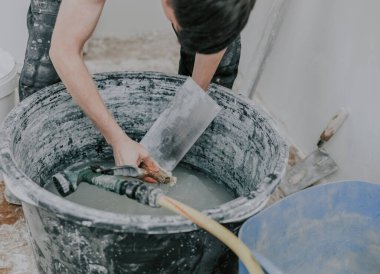 Siyah üniformalı yakışıklı beyaz adam, işi bitirdikten sonra, yakın çekimde büyük siyah bir leğende spatula yıkar. İnşaat konsepti.