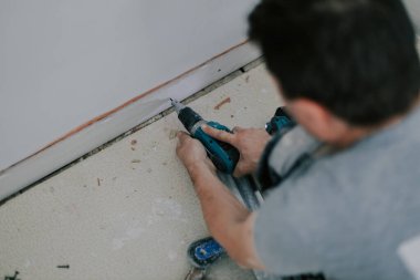 Tanımlanamayan genç beyaz bir adam vidasını ince bir tornavidayla söker, kirli bir zemine oturur, üst tarafı seçici bir odak ile kapatır. Ev yenileme konsepti