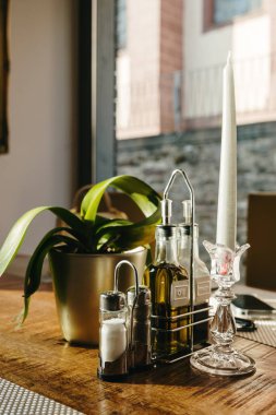 Baharatların güzel manzarası tuz, karabiber, zeytinyağı ve sirke şamdandaki mum ve saksıdaki çiçek ilkbaharda güneşli bir günde, restoranın ahşap masasında, taban manzarası, hiper yakın