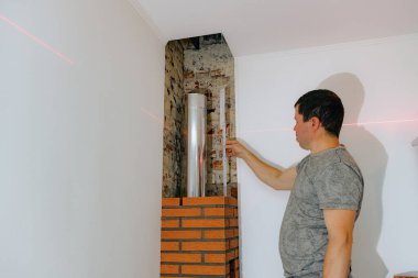 Genç yakışıklı beyaz bir adam lazer seviyesi ve cetvel seviyesini kullanır. Şöminenin bacasındaki tuğlaya yerleştirir. Seviyeyi kontrol eder, gündüzleri bir sandalyede durur ve kapatır.