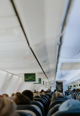View of an electronic board with a flight path, inside a flying airplane with unrecognizable people sitting with their backs in chairs, close-up side view.
