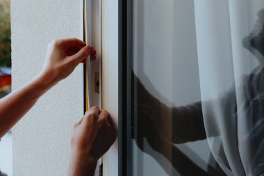 Kafkasyalı genç bir adamın elleri pencere çerçevesinin içini yalıtıyor, özel bir kauçukla yapıştırıyor, cama yansıtıyor, yakın çekim. Pencerenin onarımı ve yalıtımı için kavram