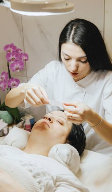 Beyaz önlüklü bir kozmetik uzmanı olan beyaz tenli güzel bir esmer kızın portresi boyama ve kirpikleri kaplama işlemine başlamadan önce bir kağıt yapıştırması yapıştırıyor.