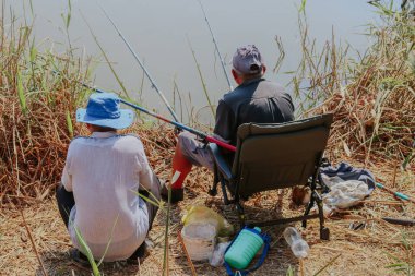 İki Kafkasyalı adam gölün kıyısında oturur ve güneşli bir yaz gününde, yakın çekim manzaralı bir oltayla balık yakalar..
