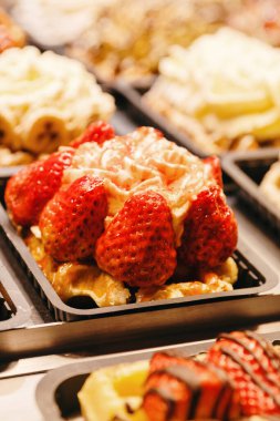 Çilekli ve kremalı Belçika waffleları gece şehrinde açık bir dükkan vitrinini dolduruyor. Belçika hamur işleri, sokak yemekleri, seyahat