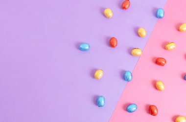 Çikolatalı Paskalya yumurtaları parlak çok renkli ambalajlarla saçılmış. Sağ arka planda eflatun pembesi, sol tarafta fotokopi alanı var. Paskalya yemeği konsepti yakın plan..