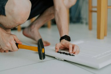 Beyaz tenli genç bir adamın elleri, beyaz bir dolaba oyulmuş siyah bir kilit takar, döşeme döşeme döşemesi üzerine çömelirken, yakın çekimde..