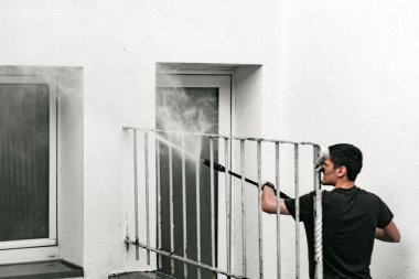 Beyaz bir adamın belden yukarısı portresi. Bir bahar günü evin arka bahçesinde bir jetle kirli metal parmaklıkları yıkıyor ve basınç altında su birikintilerini yıkıyor.