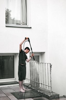 Beyaz adamın çıplak ayakla duran portresi. Baharda evin arka bahçesinde kirli metal korkulukları yıkarken. Orta ölçekli. Bahar başlangıcı konsepti