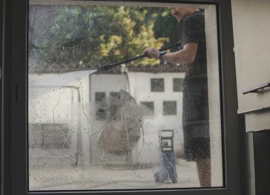 Koyu renk elbiseli beyaz bir adamın portresi avluda kirli camları temizlerken basınçlı su jeti kullanır ve bahar günü kercher kullanır. Çalışmanın ilkbahar başlangıcı kavramı