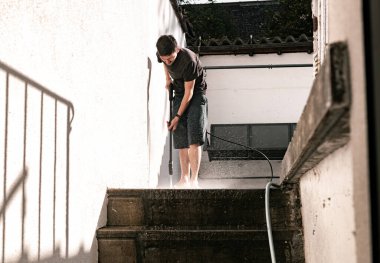 Kafkas görünümlü esmer bir gencin portresi basamakların yanında bahçe fayansları yıkıyor basınçtan uzağa uçan bir su akıntısı ile arka bahçede yamaçta duran bir yamaçta duruyor.