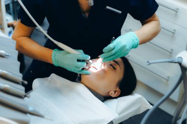 Yeşil eldivenli genç beyaz kadın dişçinin elleri dişçi matkabı kullanan güzel bir kızın ağzında plaketi temizliyor. Diş etlerinin tedavisi için kavram ve