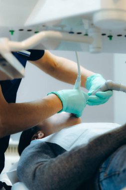 Yeşil lateks eldivenli genç beyaz dişçi özel bir klinikte diş aletleri kullanan bir kızın ağız boşluğunu seçici bir odak noktasıyla tedavi ediyor.