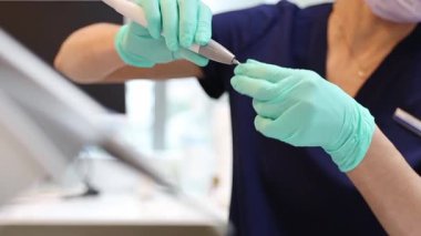 Mavi üniformalı, yeşil eldivenli, tanınmayan genç bir beyaz kadın dişçi sakız tedavisine başlamak için özel aletler hazırlıyor. Yakın plan, yan görüş.