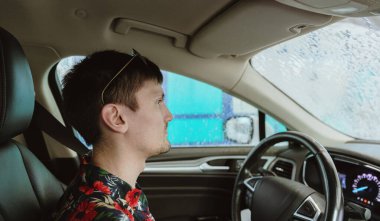 Genç, beyaz, yakışıklı, esmer bir adamın portresi. Bir bahar günü arabasını otomatik bir oto yıkamada yan yana otururken. Araba yıkama zamanı, çalışan insanlar..