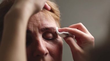 Beyaz tenli genç bir kozmetik uzmanının eli pamuk yastıkla sol kaşından geriye kalan boyayı gözleri kapalı bir kadın müşteriye kadar dikkatlice siler.