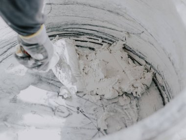 Gri uzun kollu ve eldivenli tanınmayan genç bir erkek sıva, küçük bir miktar macunu büyük, kirli bir leğenle karıştırıyor..