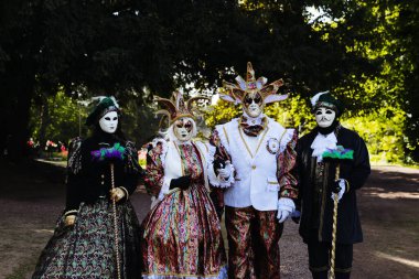 Grand Bigard Şatosu, Belçika - 27 Nisan 2025 Renkli Venedik kostümlü dört kişinin portresi kameraya bakıyor ve Maya çiçek festivali, kenar manzara, orta ölçekli sergi boyunca parkta yürüyor.