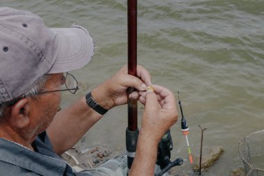 Yazın bir gölde balık tutmak için oltaya yem takan yaşlı beyaz bir adamın portresi. Balık tutma günü konsepti.