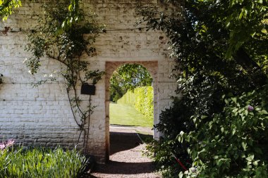Güneşli baharda, kamu parkında çiçek ve bitkilerin yetiştiği beyaz taştan bir duvarın güzel manzarası, yan görünüş. Duvarlardaki kemerler ve geçitler kavramı..