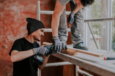 İnşaat yenileme çalışmalarının yapıldığı evde elektrikli testereyle tahta testereyle kesen iki yakışıklı beyaz adam. Seçici bir odak ile yakın çekim. Ev yenileme ve pencere konsepti