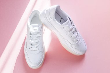 Bir çift beyaz spor ayakkabı pembe bir arka planda güneşli bir günde gölgeli bir şekilde uzanır. Moda, güzellik, ayakkabı konsepti.