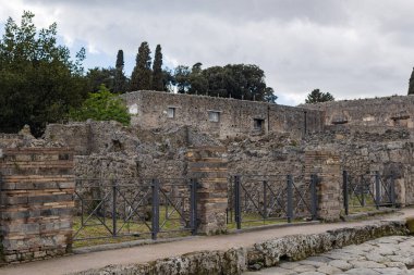 İtalya 'da bulutlu ve bulutlu bir yaz gününde antik Pompeii şehrinde modern metal kapıların eskidiği ana cadde boyunca uzanan harabelerin güzel manzarası..