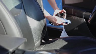 Güneşli bir bahar gününde araba yıkama yerinde deri koltuğu temizlemeden önce mavi bez üzerine kremsi cila sıkan tanınmamış beyaz bir genç adam. Yan görüntüyü yavaş çekimde çekiyor. Araba yıkamayı, çalışan insanları kavramsallaştır..