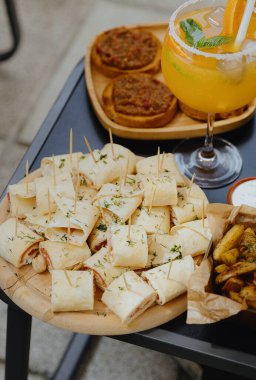 İştah açıcı aperatifler ahşap yuvarlak tabaklarda bir bardak renkli bir yaz alkollü kokteylle güneşli bir bahar gününde evin arka bahçesindeki bir masada yakın plan yan görüş..