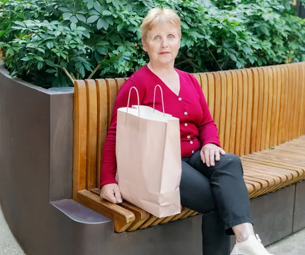 Kırmızı bluzlu güzel beyaz bir kadının portresi alışveriş merkezindeki bankta dinlenen kameraya bakan alışveriş torbaları, yan manzara, yakın çekim. Konsept, alışveriş zamanı, aile alışverişi.