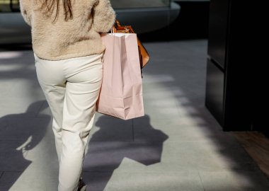 Bir alışveriş merkezinde yürürken elinde pembe bir kese kâğıdı tutan, beyaz bir kadının portresi. Konsept, alışveriş zamanı.