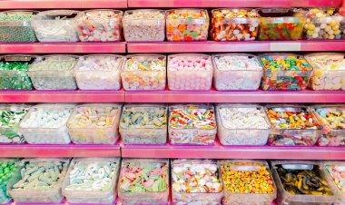 Renkli jöle şekerlerinin çok çeşitli güzel bir manzarası var. Açık plastik kutularda, bir mağazanın pembe tezgahında, yan görüntüde..