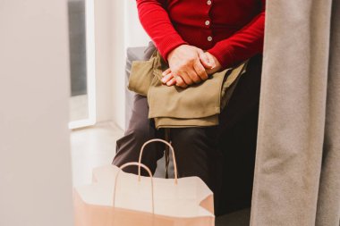 Bahar günü alışveriş merkezinin soyunma odasında uzanan pembe kese kâğıdıyla kırmızı kazaklı, tanınmayacak kadar yaşlı ve yorgun bir kadının portresi. Kavram, alışveriş zamanı, emeklilik hayatı..