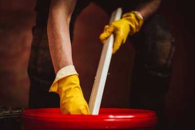 Sarı eldivenli beyaz bir genç, siyah bir evde, kırmızı bir kovanın içinde plastik bir pencere çerçevesinin bir parçasını sünger kullanarak deterjanla yıkıyor. Ev yenileme ve pencere çerçeveleri kavramı.