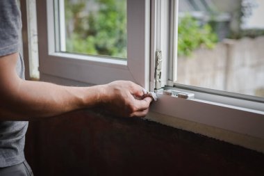 Gri tişörtlü, beyaz bir adam bahar günü odanın içinde duran kağıt peçeteyle pencerenin alt tarafını temizliyor. Pencere temizleme, pencere çerçevesi tamiri, inşaat işi.