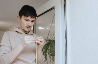 Beyaz tenli yakışıklı esmer bir adamın portresi. Kapı çerçevelerine yapıştırıcı yapıştırmak için yalıtımlı, kauçuk, kendine yapıştırıcı bir profil hazırlıyor. Pencere çerçevelerinin tamiri ve yalıtımı kavramı, bahar çalışması.