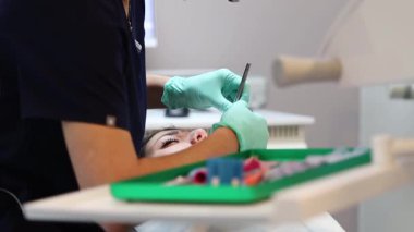 Mavi üniformalı ve yeşil eldivenli genç bir beyaz dişçi diş eti tedavisine başlamadan önce diş etlerine anestezi yapıyor. Yakın plan, yan görüş. Sakız ve diş tedavisi kavramı