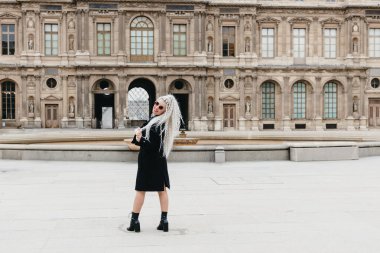 Kafasında sarı kıvırcık saçlar olan, güzel, beyaz, mutlu bir kızın portresi. Sırtından gülümseyerek kameraya bakıyor ve arka plandaki eski binanın arka planına poz veriyor. İlkbahar günü. Kavram süresi