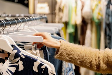 Tanımlanamayan beyaz tenli genç bir kızın bir bahar günü, sağ eliyle bir butikte askıda yaz pantolonu giydiği portresi. Alışveriş zamanını hesapla, kıyafet seç..