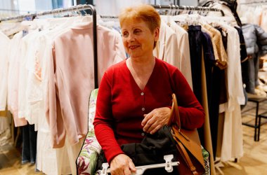 Yaşlı, güzel, beyaz, mutlu, kırmızı bluzlu bir kadının portresi. Koltuğunda oturan, elinde bir şey olan ve bahar günü butikte yüzünü çeviren mutlu kadın. Alışveriş zamanı, kıyafet seçimi..