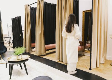 Tam boy portresi, genç, beyaz bir kızın bahar günü butikte yeni bir elbise aynasına bakarken, yan görünüş yakın. Alışveriş zamanı konsepti, insanların yaşam tarzı..