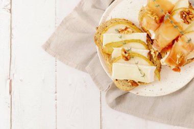 İki sağlıklı sandviç, armut, peynir, fındık, bal, kurutulmuş dilimler ve mısır gevreği ekmeğinde bir dal biberiye, sağdaki peçetede duran bir tabakta beyaz ahşap bir masanın üzerinde, tarlanın derinliği ile çok yakın bir şekilde yatıyordu. Sağlıklı gıda konsepti.