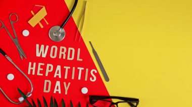 Bir stetoskop, beyaz haplar, sarı ve kırmızı kurdele, gözlük, cerrahi aletler, palmiye yaprağı ve hafif tahta harfler hizalı dünya Hepatit Günü sol tarafta kırmızı ve sarı parlak bir arka planda duruyor, sağ tarafta düz, düz bir kopya alanı var.