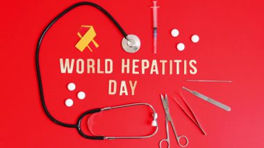 Bir stetoskop, beyaz haplar, sarı ve kırmızı bant, şırınga, cerrahi aletler ve hafif ahşap harfler hizalı dünya Hepatit Günü kırmızı arka planda yatar, düz çekimde yakınlaşır, yavaş çekim.