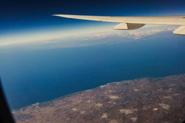 Güzel bir mavi deniz manzarası ve karanın bir kısmı yaz mevsiminde uçak penceresinden içeri doğru bir kanat, yakın bir yan manzara..