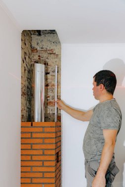 Genç yakışıklı beyaz bir adam lazer seviyesi ve cetvel seviyesini kullanarak şöminenin bacasındaki bir tuğlaya yerleştiriyor, düzlüğü kontrol ediyor, gün boyunca bir sandalyede duruyor, seçici bir odak ile yan görüş sağlıyor. Temiz tuğla işi