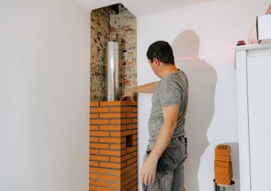 Genç yakışıklı beyaz bir adam şöminenin şömine bacasına tuğla dökerken gün boyunca bir sandalyede dikilirken, seçici bir odak ile yakın plan yan görüş. Temiz tuğla işi konsepti, ev yenilemesi..