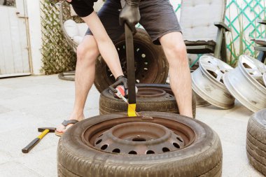 Bir bahar günü arka bahçede dikilirken, bir araba tekerleğinden eski bir lastiği çıkarmak için levye ve sıvı sprey kullanan yarı tanınmış genç bir adamın portresi. Araba lastiklerini çıkarma, tekerlek tamiri kavramı.