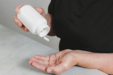 Son sınıf tanınmayan bir kadının portresi şişeden avucuna ilk beyaz kapsül tabletini dolduruyor. Gündüz vakti masada oturuyor. Yakın plan. Haplanma süresi ve emeklilik hayatı kavramı.