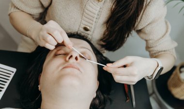 Bir bahar günü ofiste kozmetoloji masasında uzanan bir bayan müşterinin sol gözündeki doğal kirpikleri iki rulo dikkatlice temizleyen tanınmamış beyaz kozmetikçinin portresi. Konsept